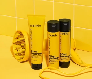 Matrix A Curl Can Dream hair products next to a yellow diffuser and hair dryer against yellow tiles