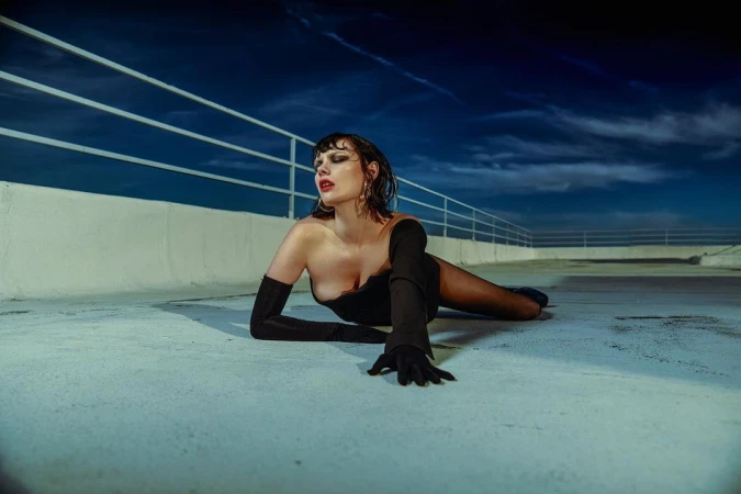 Woman in a black dress and long gloves lying on a concrete rooftop under a dark night sky by Alexandre Bassard