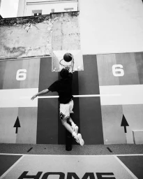 Basketball player mid-air dunking a basketball on an outdoor court with painted walls and arrows.