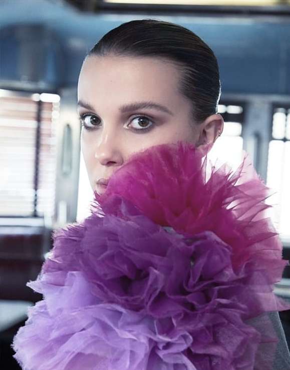 Close-up studio portrait of an adult female wearing a pink and purple ruffled neckpiece, and with her hair pulled back.