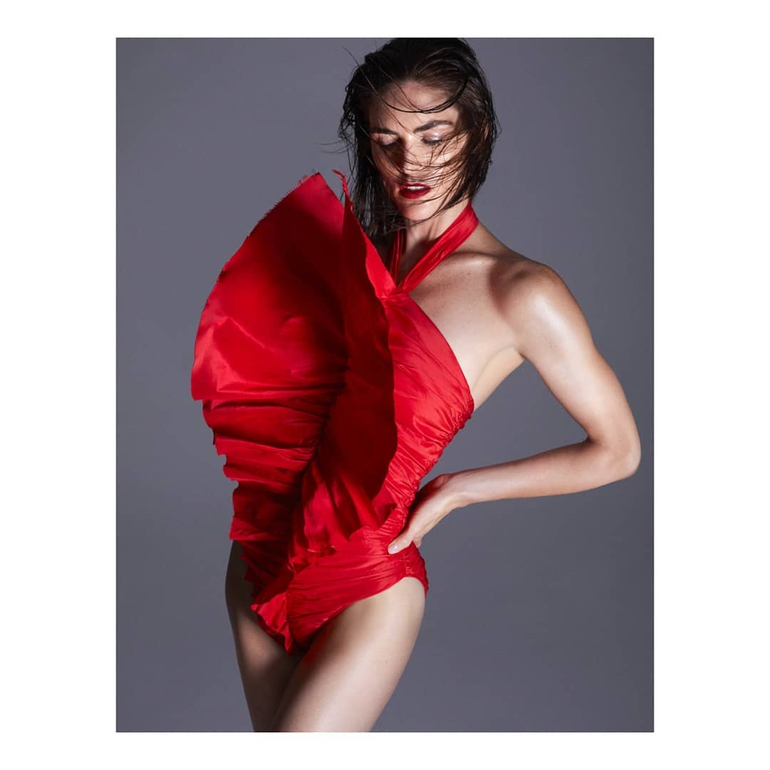 Elegant adult woman in a red one-piece swimsuit poses in a studio setting. Soft studio lighting highlights her features and the garment's texture.