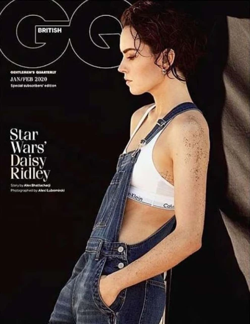 Daisy Ridley cover for British GQ, wearing denim overalls and a white Calvin Klein top, against a dark background in a studio.