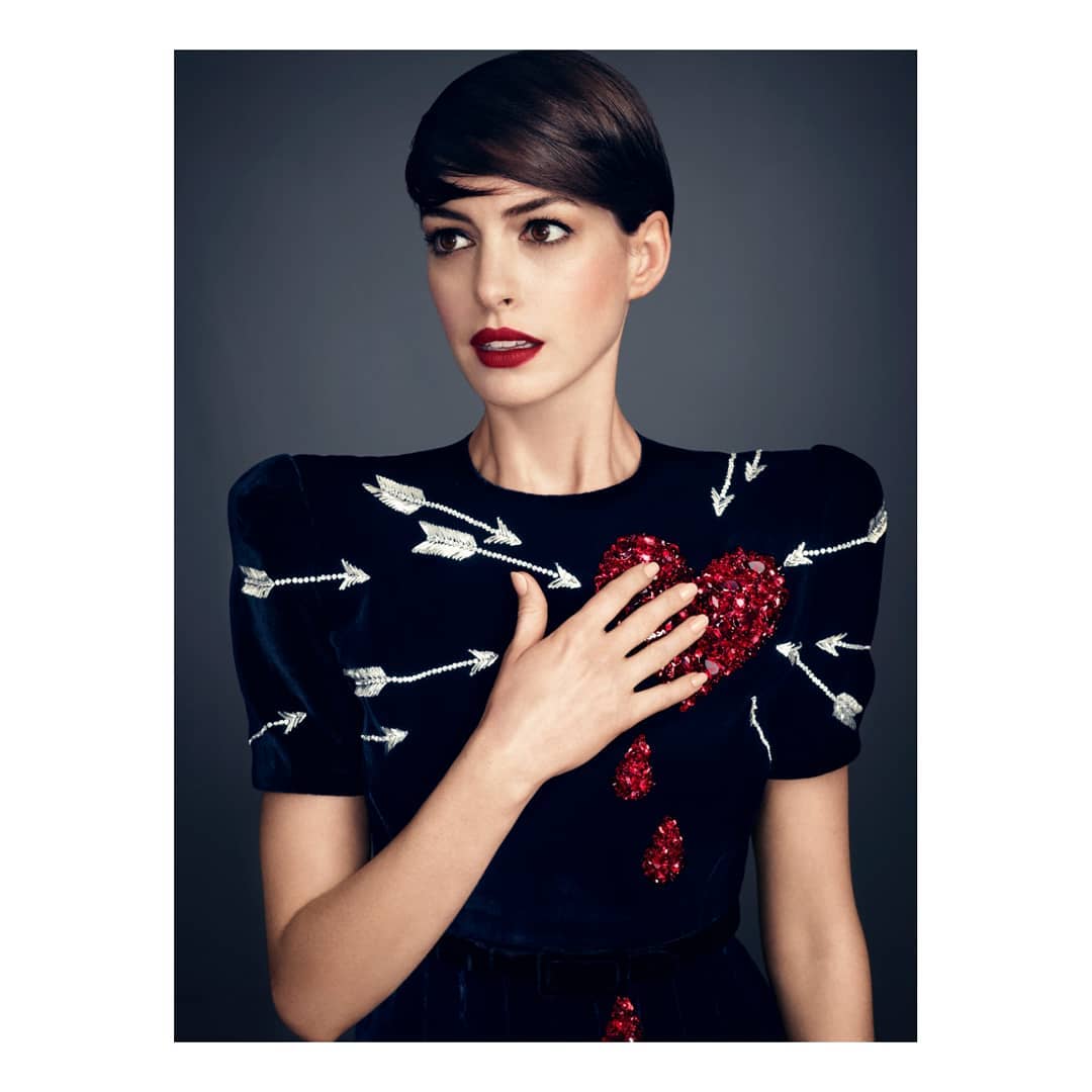 Close-up portrait of adult woman with short dark hair, wearing a navy blue dress embellished with arrows and a heart design.