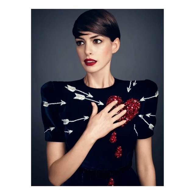 Close-up portrait of adult woman with short dark hair, wearing a navy blue dress embellished with arrows and a heart design.