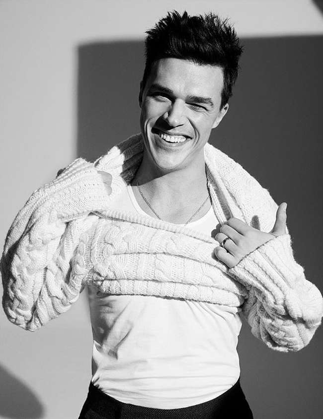 Portrait of a smiling adult male wearing a white shirt, with a knitted sweater draped over his shoulders in a studio setting.