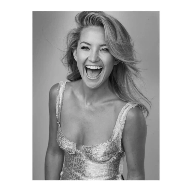 Black and white portrait of a blonde woman with a wide smile, wearing a sparkly top, against a plain background.
