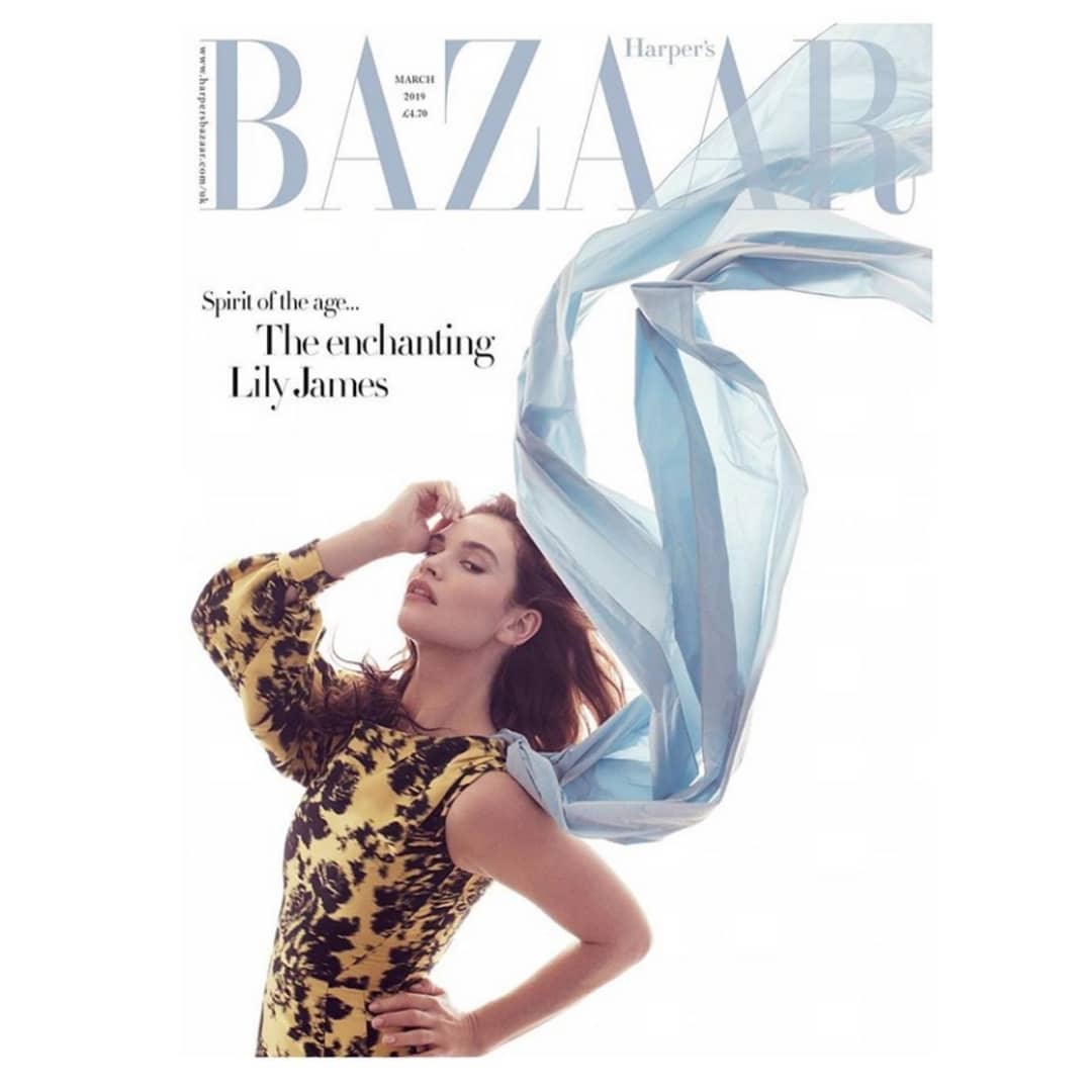 Lily James, actress, poses on the cover of Bazaar magazine wearing a yellow floral dress and a blue sheer scarf against a white background.