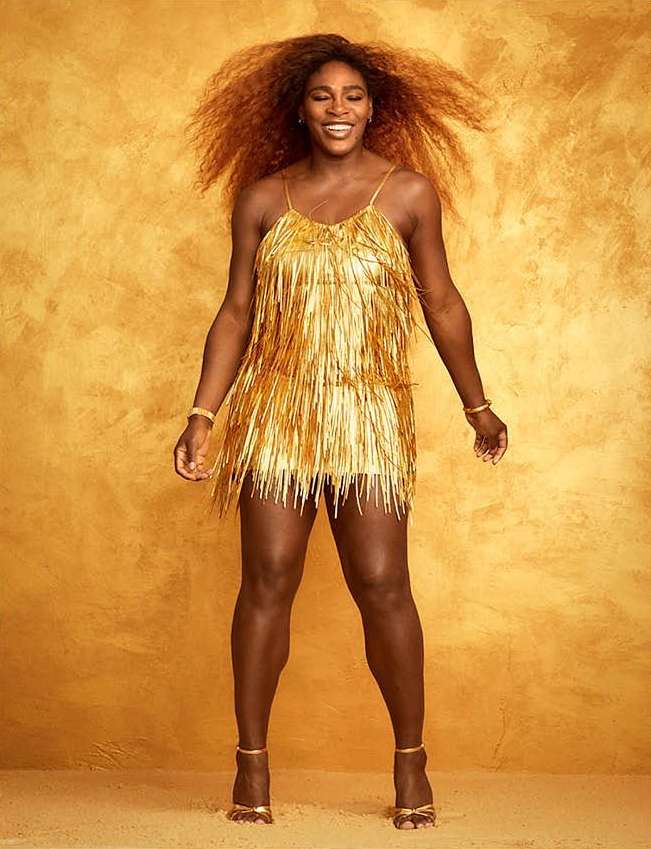 Serena Williams poses in a gold fringe dress and heels against a textured golden backdrop, smiling with radiant energy. 