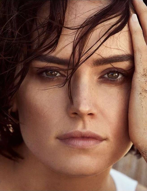 Close-up portrait of a woman with brown hair and eyes, her hand touching her face, against a soft, blurred background.