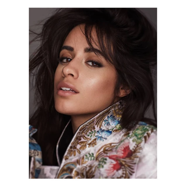 Close-up portrait of a young adult woman with dark hair and light skin, wearing a colorful patterned jacket, looking at the camera.