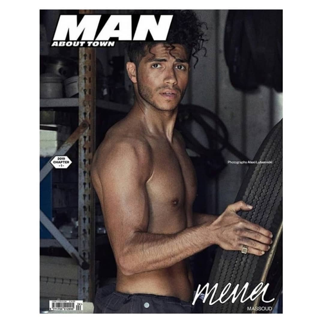 Magazine cover featuring Mena Massoud shirtless, holding tire, with 'Man About Town' title, shot indoors with visible garage-like background.