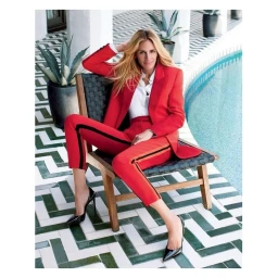 Julia Roberts in a red pantsuit sitting on a woven patio chair by a swimming pool