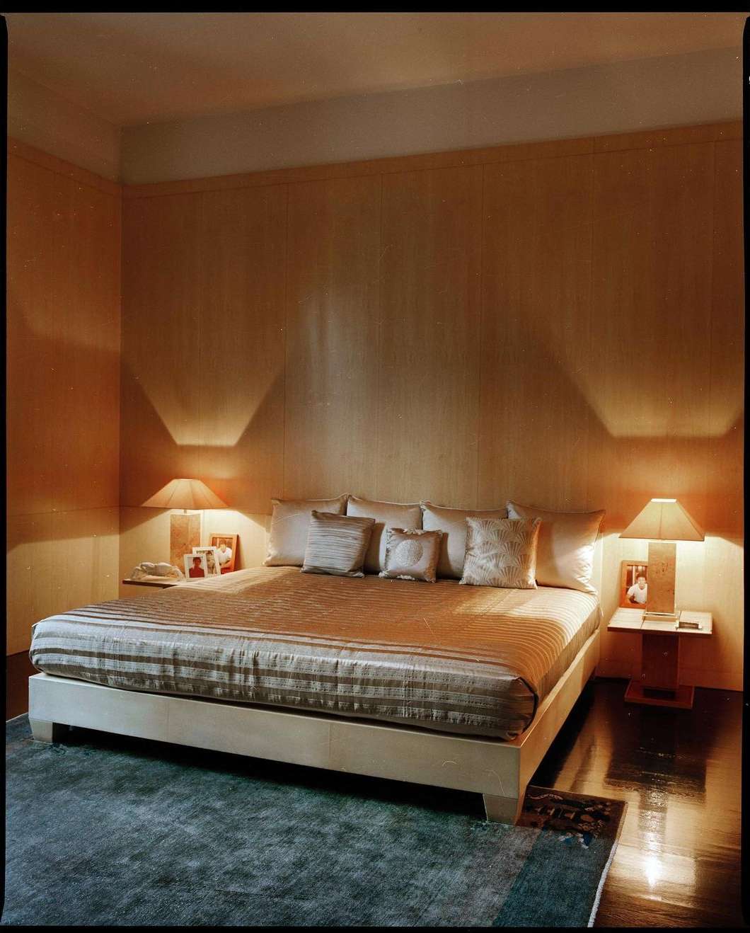 Bedroom interior with a bed, pillows, lamps, and wooden walls, creating a cozy and inviting atmosphere for relaxation and rest.