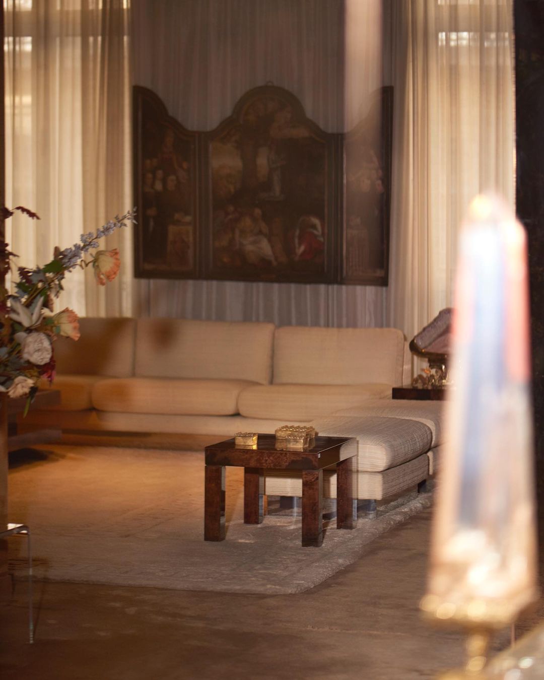 Interior view of a living room with a long cream sofa, wooden coffee table on a gray rug, and a large painting on the wall.