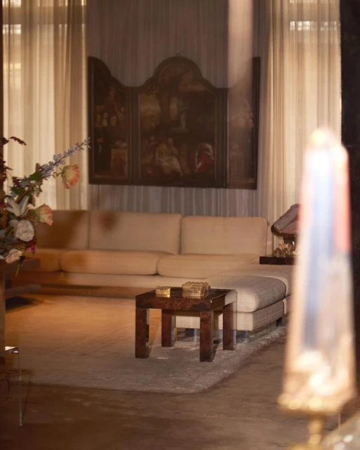 Interior view of a living room with a long cream sofa, wooden coffee table on a gray rug, and a large painting on the wall.