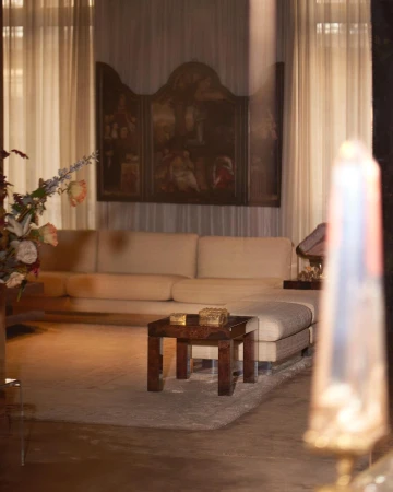 Interior view of a living room with a long cream sofa, wooden coffee table on a gray rug, and a large painting on the wall.