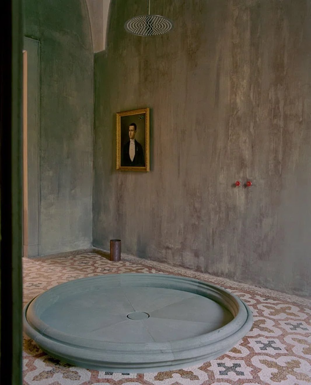Artistic bathroom interior with a unique round shower base, patterned tile floor, and a framed portrait on the textured wall.