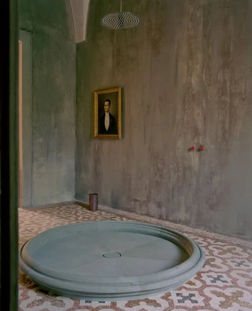 Artistic bathroom interior with a unique round shower base, patterned tile floor, and a framed portrait on the textured wall.