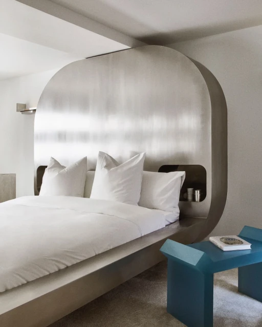 Modern bedroom interior with a platform bed, white bedding, minimalist silver headboard, and turquoise side table, creating a serene space.