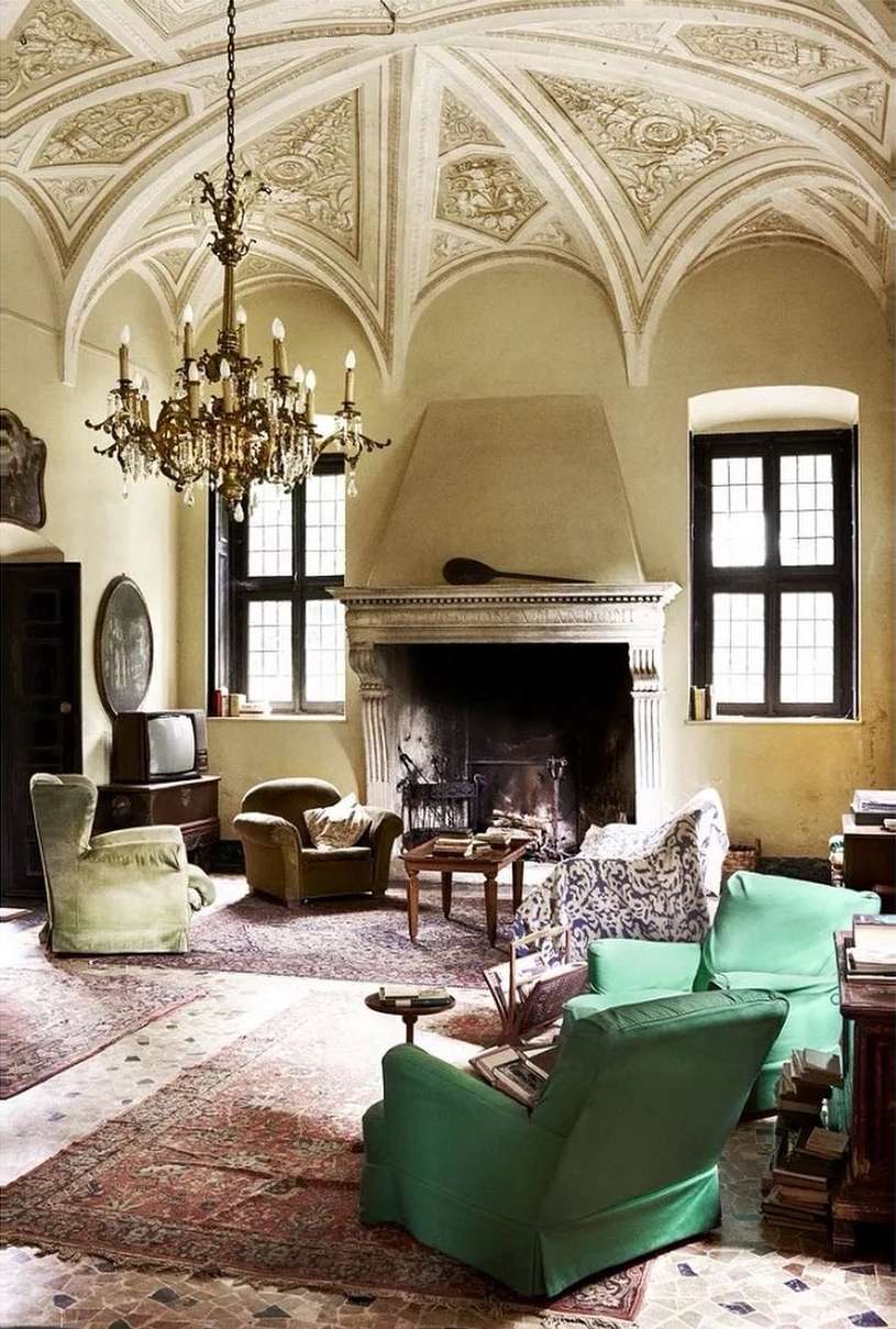 Interior of a living room featuring vintage armchairs, a fireplace, and a chandelier, set against a background of ornately decorated walls and ceilings.