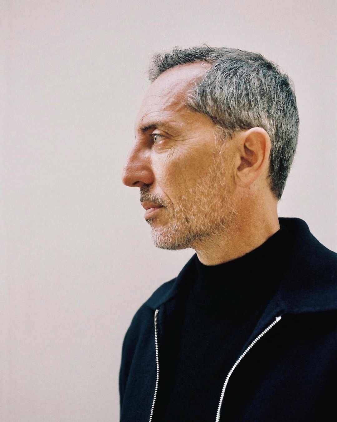 Profile portrait of a man in his 50s wearing a black zip-up jacket against a light plain background
