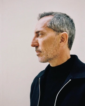 Profile portrait of a man in his 50s wearing a black zip-up jacket against a light plain background