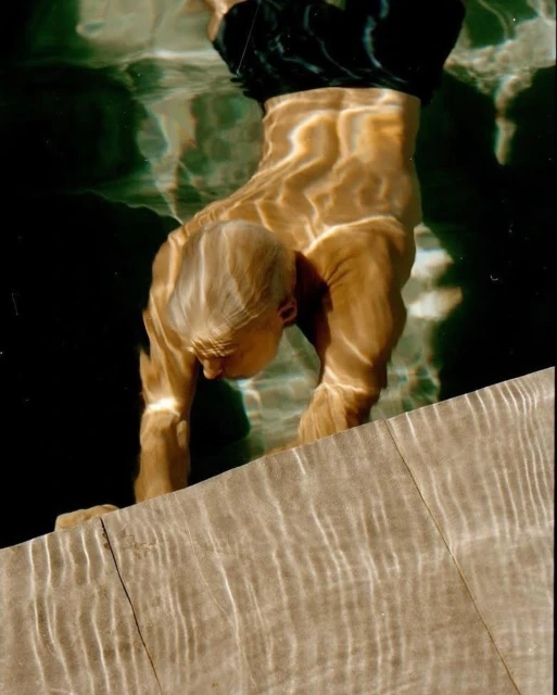 Underwater shot of an adult male in a swimming pool, showcasing distorted light patterns and tiled pool edge.