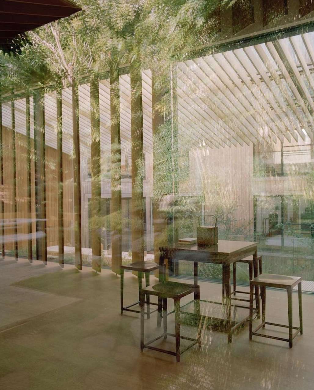 Indoor scene featuring a dark wooden table and four stools. The interior space has an open feel, with a window view of outdoor foliage.