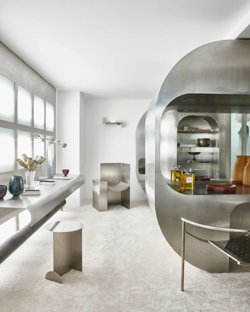 Minimalist interior design featuring metal furniture, rounded shelves with perfume, vases with dried flowers, and soft lighting.