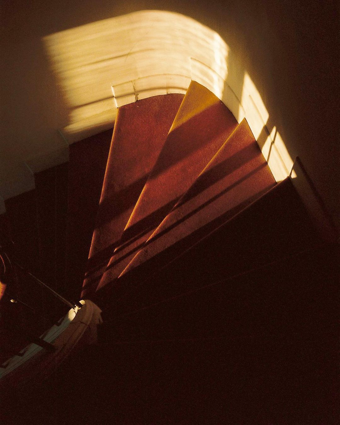 Carpeted spiral staircase in a dark interior illuminated by a soft, golden light streaming down from above.