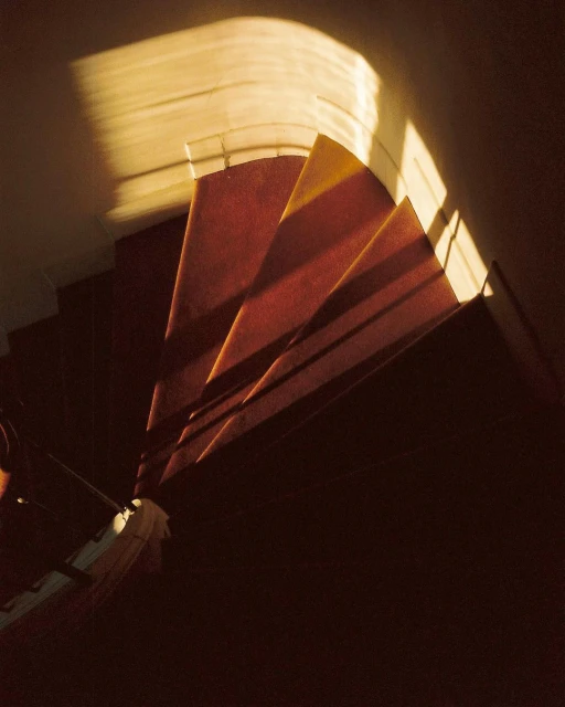 Carpeted spiral staircase in a dark interior illuminated by a soft, golden light streaming down from above.