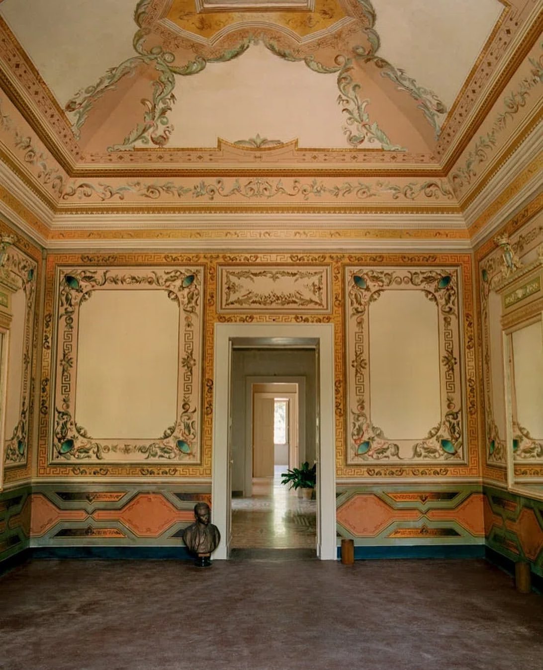 Ornate interior featuring decorative wall panels, ceiling art, and a classical bust in a historic building with an open doorway.
