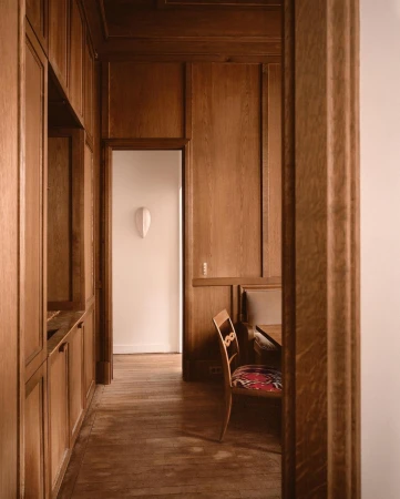 Interior design of a wood-paneled room featuring a vintage-style chair and a glimpse into a white-walled area with a wall sculpture.