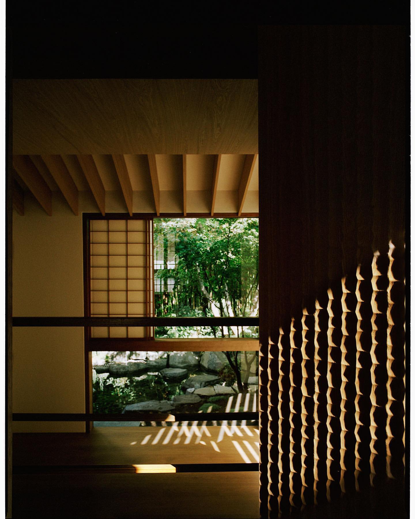 Interior view of a traditional Japanese room with tatami mats, shoji screens, and an exterior garden visible through the window.