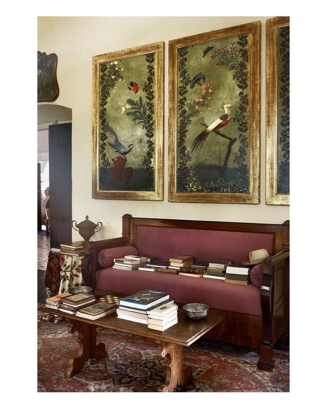 Living room interior with a burgundy sofa, a wooden coffee table with books, and three framed bird paintings on a white wall.