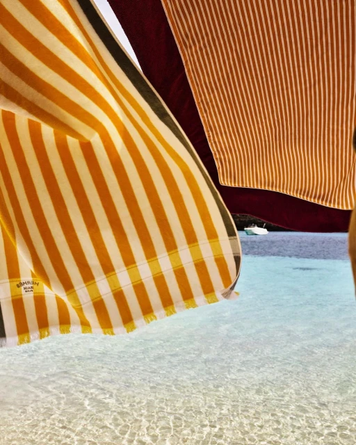 Beach photo of yellow and white striped towels with water and boat. Striped fabric pattern. Nautical beach towel. Textile background.