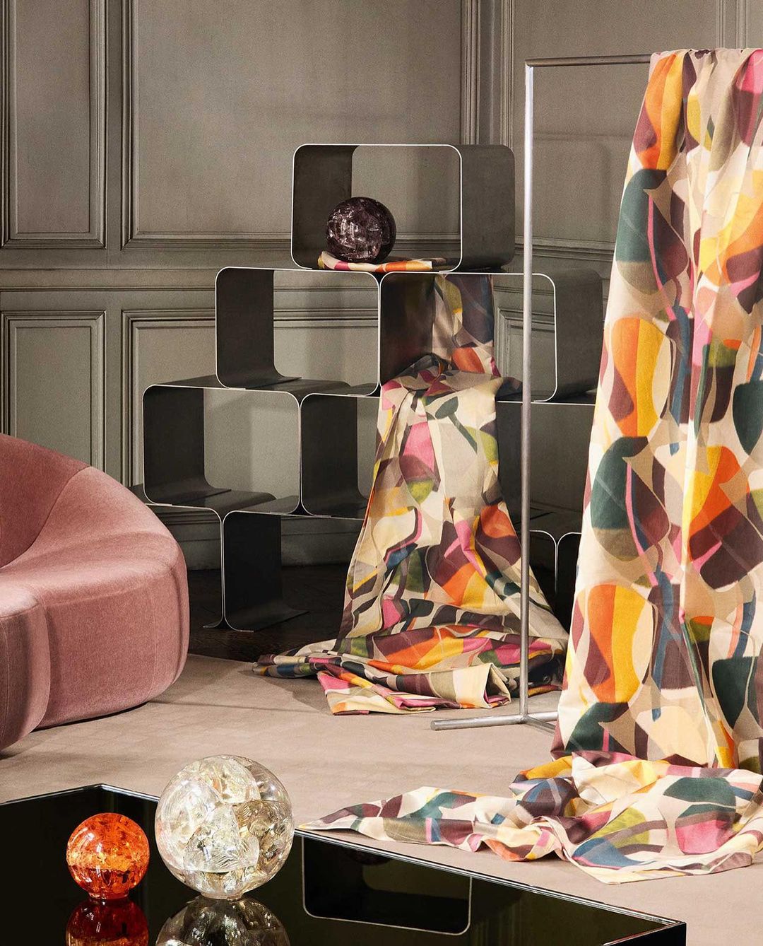 Interior showcase featuring a modern rounded lounge chair, geometric shelving with decorative objects, and a patterned textile drape.