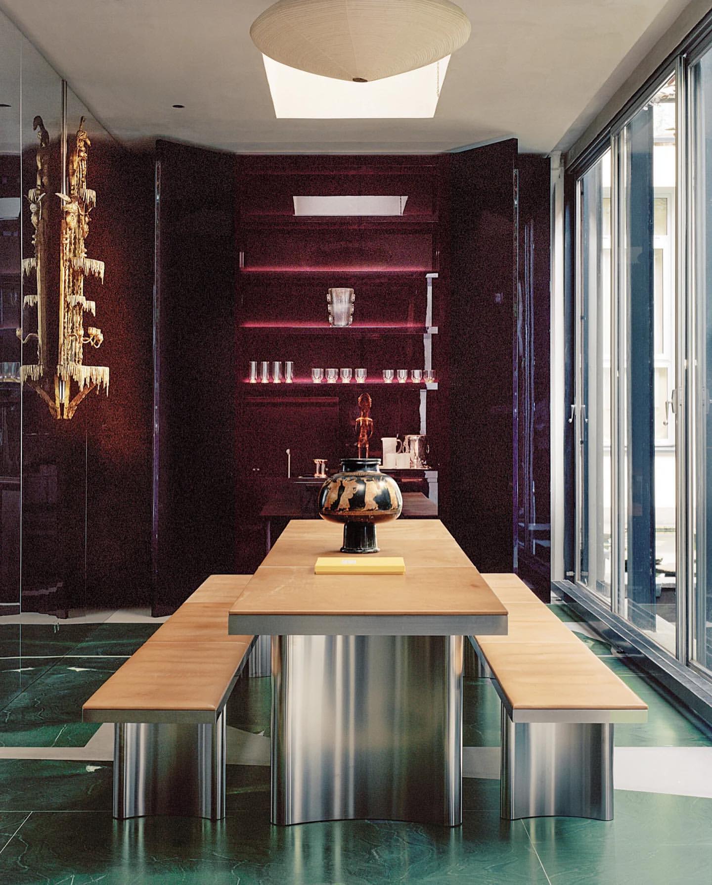 Modern interior with wooden dining table and benches featuring metal bases, set against a backdrop of dark walls and marble flooring.