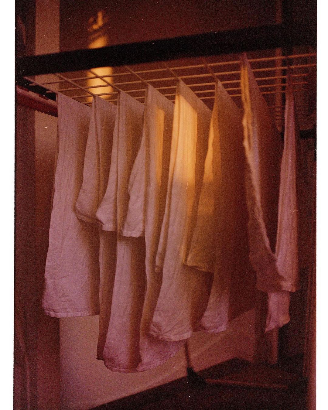 Laundry drying on a metal rack indoors. White garments hang evenly spaced in a brightly lit, domestic setting. Simple domestic scene.