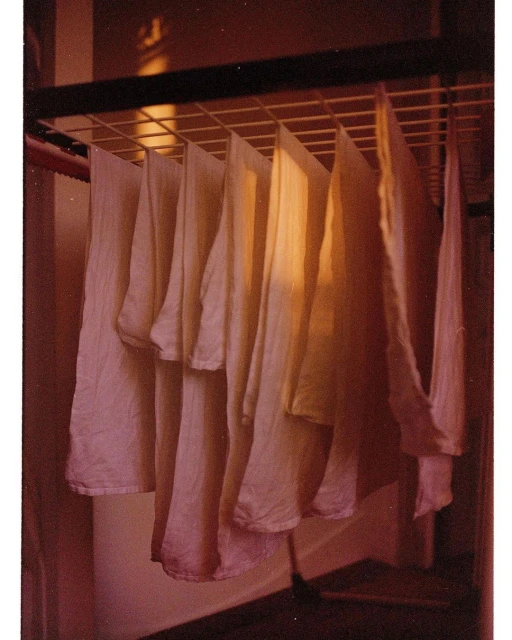 Laundry drying on a metal rack indoors. White garments hang evenly spaced in a brightly lit, domestic setting. Simple domestic scene.