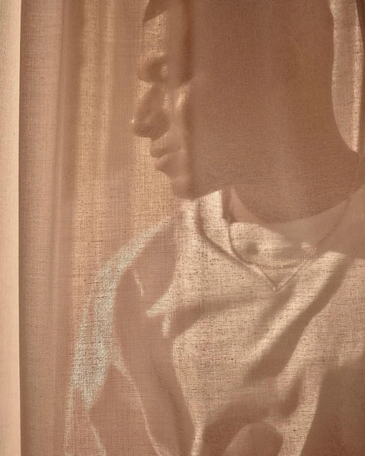 Portrait of a contemplative adult male bathed in soft, diffused natural light through a linen curtain, creating a serene and intimate atmosphere.