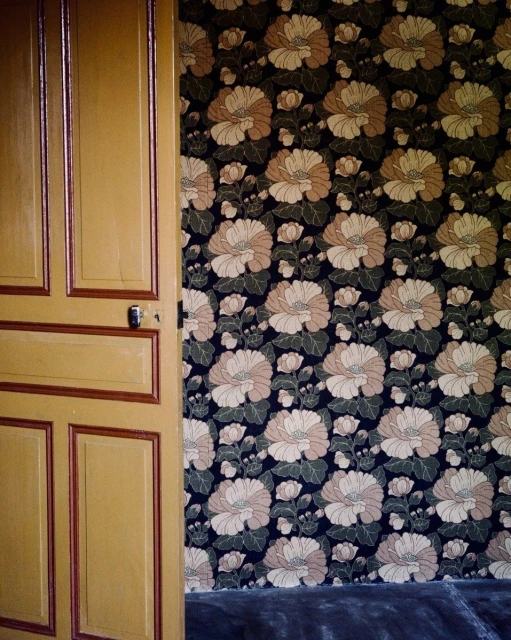 Floral wallpaper with a retro pattern decorates an indoor room, accented by a yellow door, creating a warm and inviting visual.