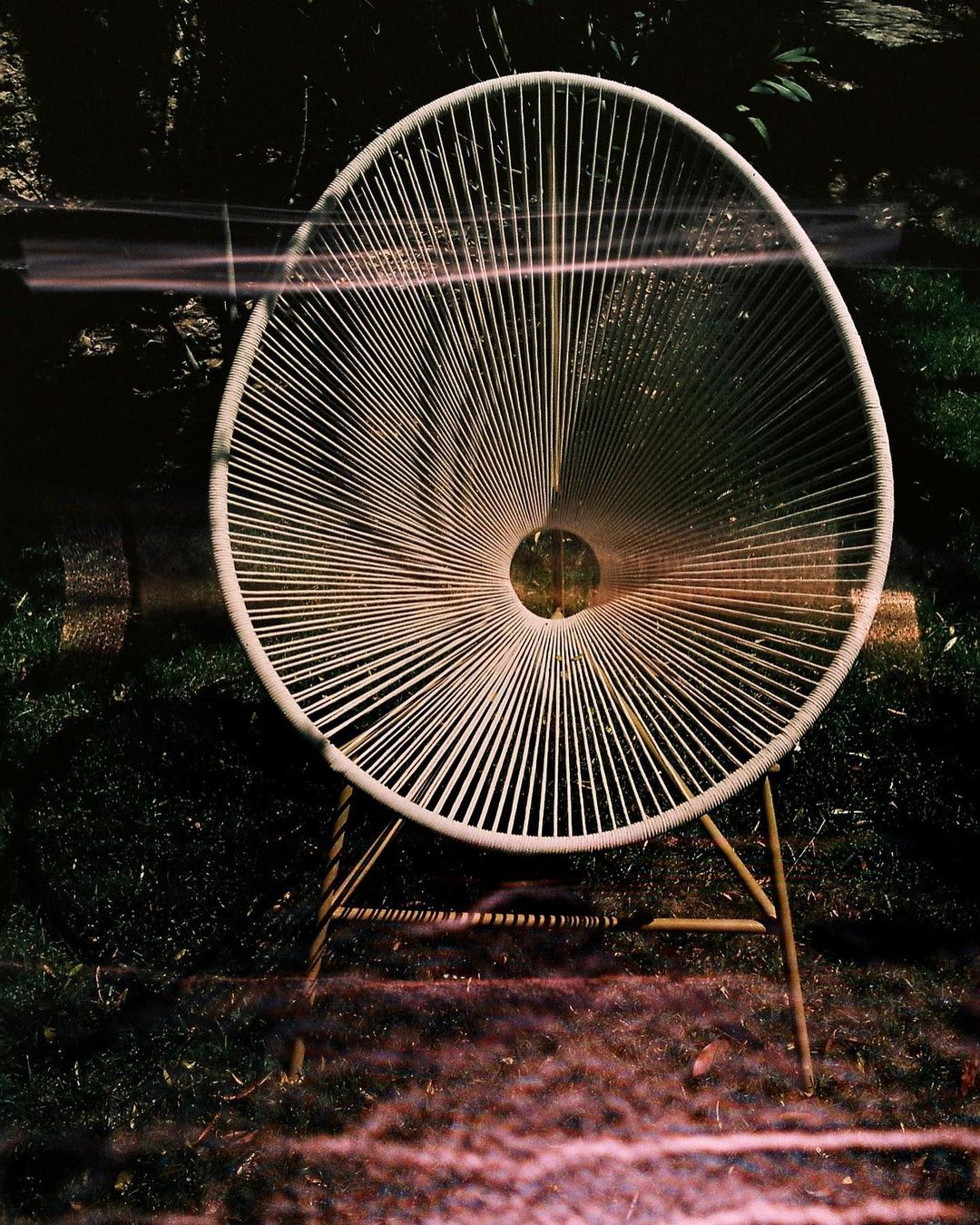 A white string lounge chair outdoors in a garden setting photographed by Alexis Armanet in Paris