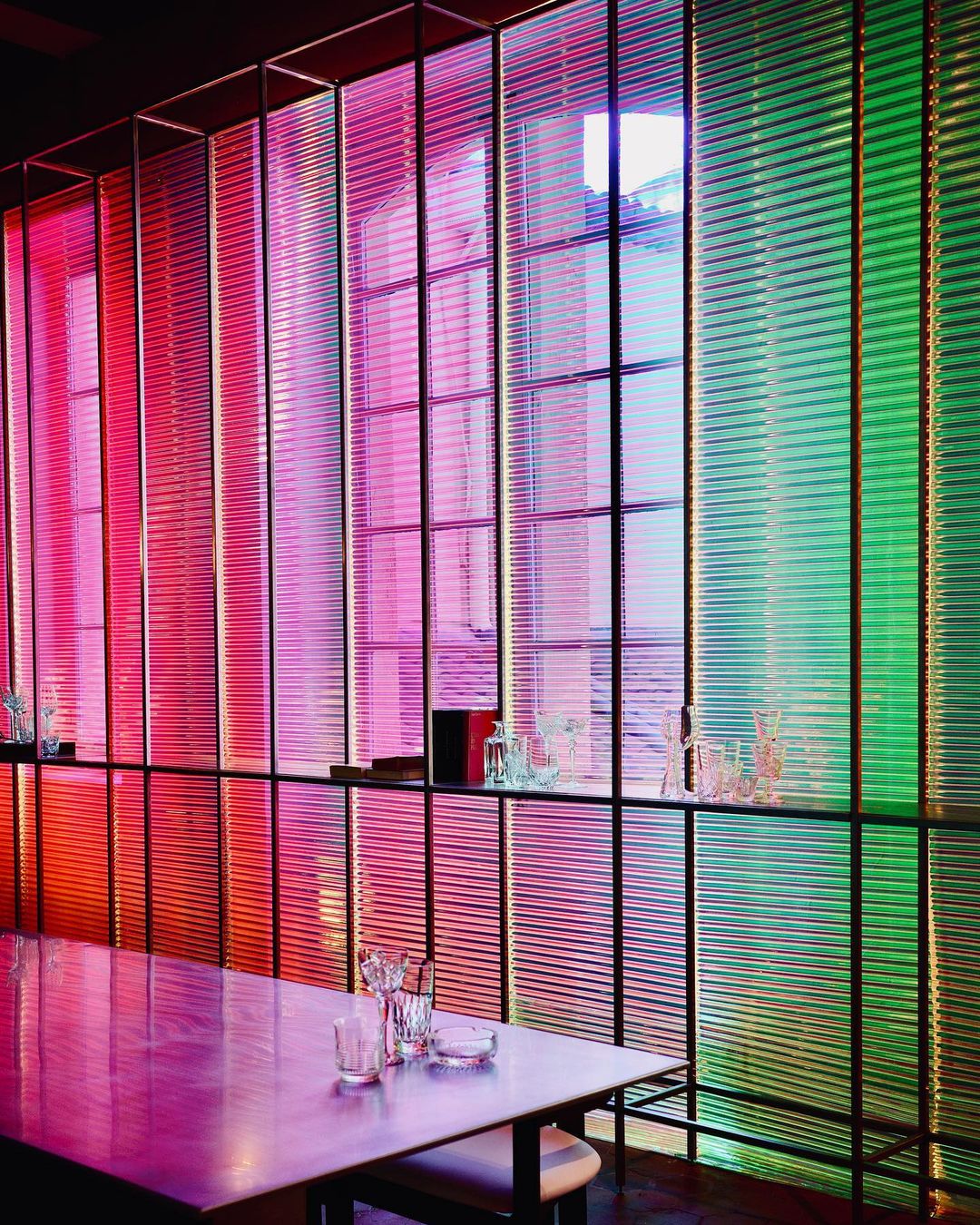 Architectural interior with window blinds in gradient shades of orange, pink, blue and green. Table setting in the foreground.