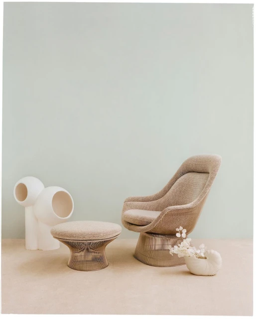 Interior design featuring a beige swivel chair, matching ottoman, white decorative sculpture, and small vase with white flowers.