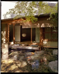Traditional Japanese building exterior with a wooden porch over a koi pond containing several visible fish.
