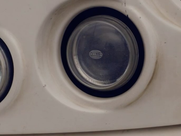 Close-up of a white automotive headlight with the brand name HELLA visible, showing the design and details of the car part.