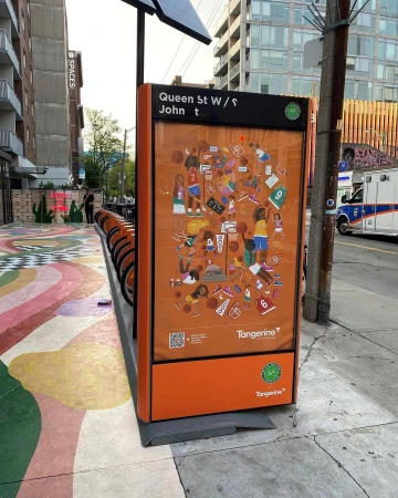 City street scene featuring a public bike rack station with an orange advertisement panel displaying basketball-themed artwork.