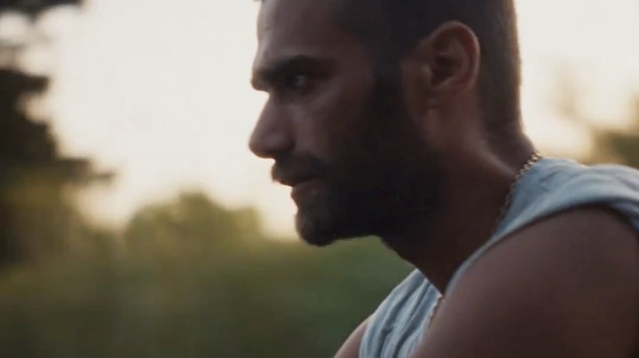 Close-up profile of an adult male with a beard and tank top. Natural lighting and outdoor environment create a contemplative portrait.