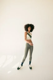 Woman with afro hair wearing a colorblocked crop top and olive green leggings posing in a bright studio.